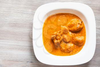 Indian cuisine - Murg Makhan Masala barbequed chicken pieces in spicy tomato and creamy curry sauce in white bowl on wood board