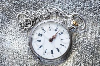 two minutes to twelve o'clock on antique pocket watch on silver fabric background