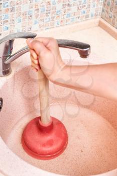 woman clears kitchen sink drain by rubber plunger