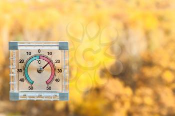 outdoor thermometer on home window and blurred yellow trees on background in sunny warm autumn day