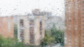 rain drops on window glass and blurred cityscape on background on rainy autumn day