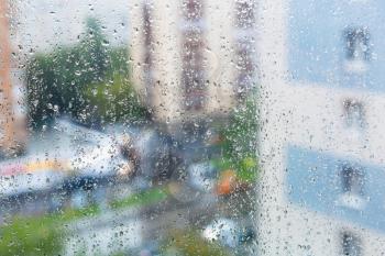 raindrops on window glass and blurred city street on background on rainy autumn day