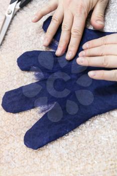 workshop of hand making a fleece gloves from blue Merino sheep wool using wet felting process - craftsman puts fibers on fingers of wet glove