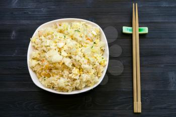 Chinese cuisine dish - top view of served portion of Fried Rice with Shrimps, Vegetables and Eggs (Yangzhou rice) with chopsticks on dark wooden table