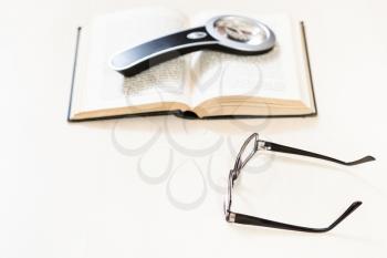 reading book with low vision - spectacles and magnifying glass on open book on pale table (focus in the foreground)