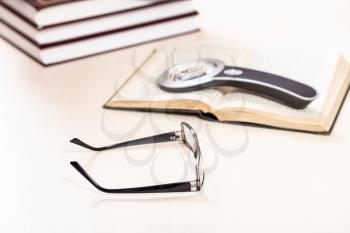 reading book with low vision - glasses and loupe on open book near stack of books on pale table (focus in the foreground)
