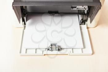 sheets of blank white paper in printer tray of multi function device on table in office