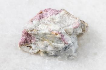 macro photography of sample of natural mineral from geological collection - unpolished pink Tourmaline mineral in feldspar and quartz rock from Kalba Range, Kazakhstan on white marble background