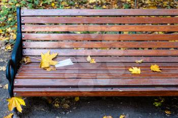 thrown medical face fask on wooden bench in city park on autumn day