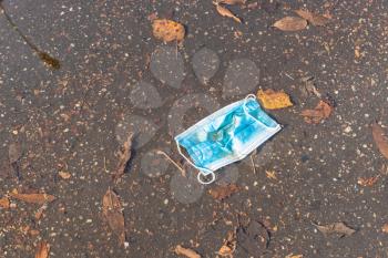 thrown sanitary face mask floats in puddle with fallen leaves on sunny autumn day