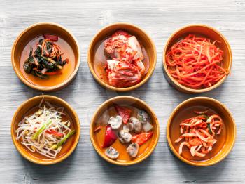 korean cuisine - top view of various appetizer (Banchan or Panchan) in ceramic bowls on gray table