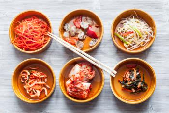 korean cuisine - chopsticks above various appetizers (Banchan or Panchan) in ceramic bowls on gray table