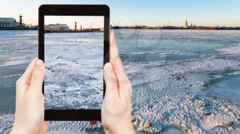 travel concept - tourist photographs of frozen Neva river and Spit of Vasilyevsky Island with Rostral Column and Old Stock Exchange building in Saint Petersburg city in Russia on smartphone in spring