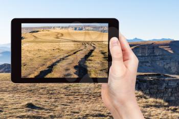 travel concept - tourist photographs of dirty road on top of Bermamyt mountain Plateau at september morning in North Caucasus region of Russi on smartphone