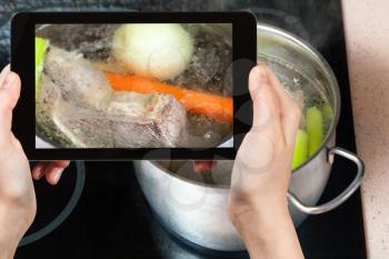 travel concept - visitor photographs of cooking soup with boiling beef broth in steel stewpan close up on caramic stove on smartphone