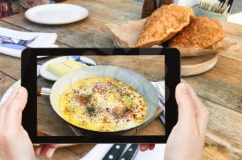 travel concept - visitor photographs of Fried Eggs with Sour Cream in Kabardian style in pan and hominy in local restaurant in North Caucasus region of Russia on smartphone