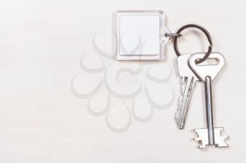 pair of door keys on keyring with blank white keychain on pale brown table