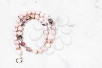 coiled necklace from cherry blossom rose quartz beads on gray concrete surface with copyspace