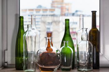 many empty bottles on windowsill and view of city through home window on background