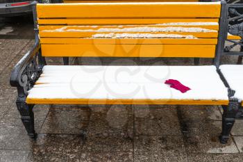 yellow wooden bench covered by snow with red female glove on Manezhnaya square in Moscow city in winter