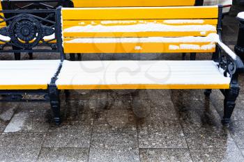 front view of yellow wooden benches under snow on Manezhnaya square in Moscow city in winter