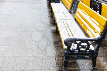 yellow wooden benches covered by snow on wet pavement of Manezhnaya square in Moscow city in winter