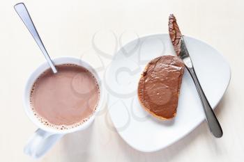 top view of cup with hot chocolate and toast with chocolatte spread on plate on table