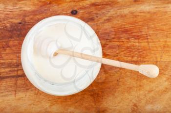 top view of honey spoon in glass jar with natural organic white honey on wooden board