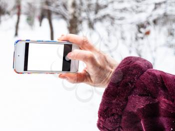 female hand takes picture by smartphone with cutout screen in winter forest