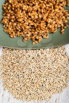 top view of raw whole rye grains and boiled porridge on green plate close up on wooden table