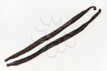 top view of two different whole vanilla beans (tahitian vanilla and bourbon vanilla) on white plate