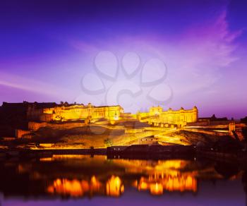 Vintage retro hipster style travel image of Amer Fort (Amber Fort) illuminated at night - one of principal attractions in Jaipur, Rajastan, India refelcting in Maota lake in twilight