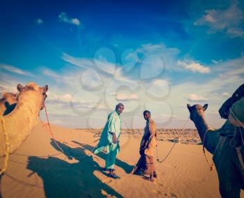 Vintage retro hipster style travel image of Vintage retro hipster style travel image of Rajasthan travel background - two indian cameleers (camel drivers) with camels in dunes of Thar desert. Jaisalme