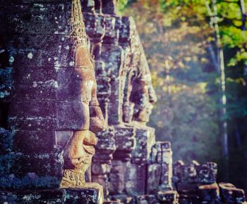 Vintage retro effect filtered hipster style travel image of Ancient stone faces of Bayon temple, Angkor, Cambodia on sunset