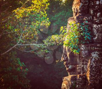 Vintage retro effect filtered hipster style travel image of ancient stone face of Bayon temple, Angkor, Cambodia with growing plants