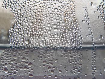 Monochrome water drops on a transparent glass surface taken closeup as background.