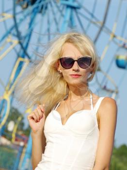 Pretty blonde with sun glasses against carousel and blue sky.