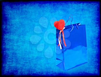 Blue Valentines Day gift bag and red heart on blue grungy background with empty space.