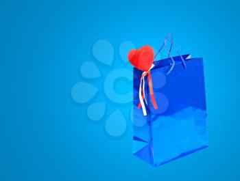 Blue Valentines Day holiday gift bag and red heart on blue background with empty space.