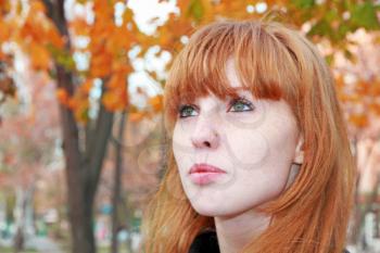 Pretty red hair girl face with freckles against red autumn foliage.
