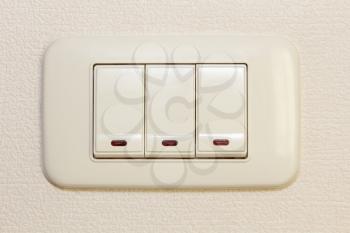 Threefold multiply light switch on beige wall taken closeup.
