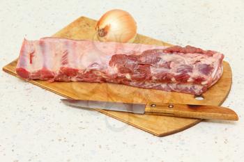 Raw pork ribs,knife and onion on wooden cutting board taken closeup.