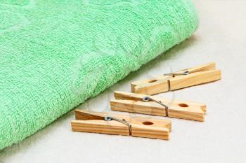 Green towel and wooden clothespins on white fabric background.
