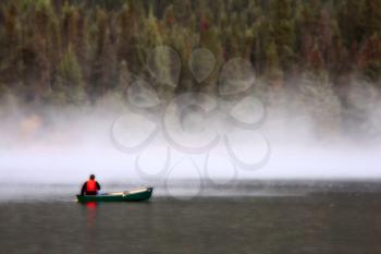 Man in canoe near morning mist on lake