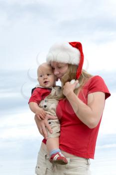 Young attractive mom with Santa's hat and the little baby on the cloudy sky background
