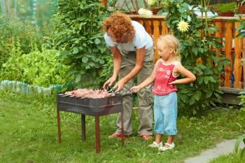 Little girl helping her mother to cook shish kebab for a picnic outdoors
