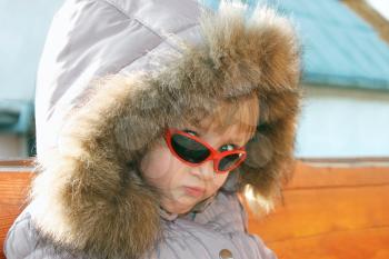 Portrait of cute little girl in sunglasses and winter hood outdoors