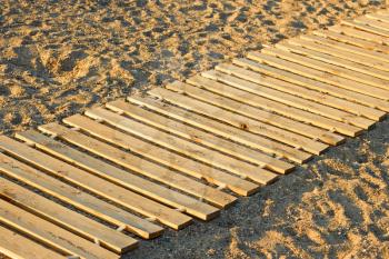 Long wooden mat made from new parallel planks lying on a sandy beach