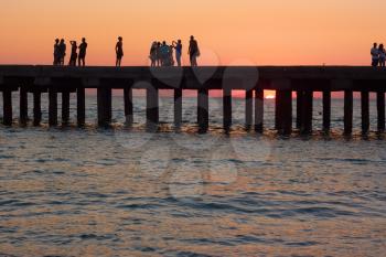 Groups of people on the old pier are photographed and admire the beautiful sunset over the Black Sea coast in Crimea, Ukraine