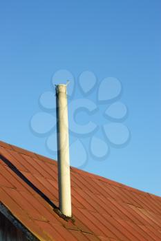 Chimney on an old tinny roof against the blue sky